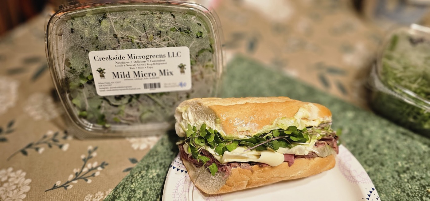 A sandwich topped with fresh microgreens next to a packaged Mild Micro Mix container